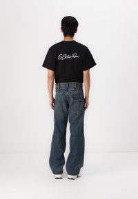 T-shirt noir à manches courtes avec le texte blanc "G-Star Raw" au dos, associé à un jean en denim bleu ample avec des coutures et des poches distinctes.