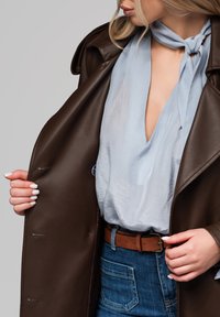 Brązowy skórzany płaszcz, jasnoniebieska jedwabista koszula, dżinsy z widocznymi kieszeniami, brązowy pasek z metalową klamrą, gładkie tekstury i akcenty.