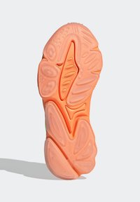 Kengän pohja eloisan oranssista kumista, jossa on erilaisia kuvioituja pintoja, kuten uurteita ja pyöreitä painaumia, jotka on suunniteltu lisäämään pitoa.