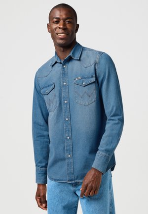 Denim shirt in light blue with a standard collar, two chest pockets, and contrasting stitching. Long sleeves with button cuffs.