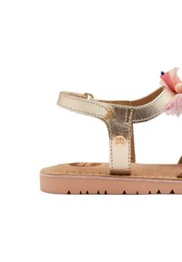 Sandalia metálica dorada con diseño de tira en T, plantilla de gamuza suave y acentos florales en rosa. Suela texturizada con muescas para un mejor agarre.