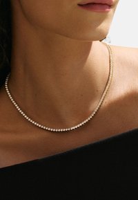 Halskette in goldfarbener Ausführung mit einer filigranen Kette, die dicht gesetzte, klare Edelsteine aufweist, sowie einer geschwungenen Form und glatter Textur. Geeignet für formelle Kleidung.