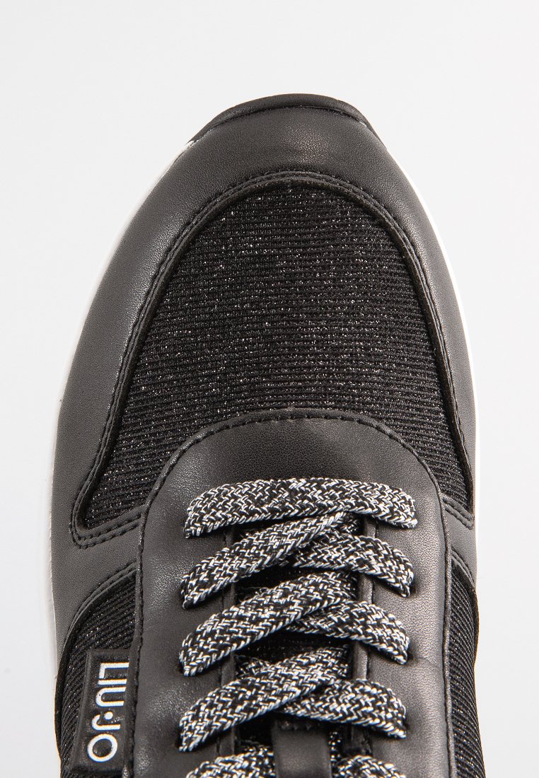 Baskets noires avec un dessus en tissu texturé, des accents en cuir synthétique et des lacets gris avec un motif réfléchissant.
