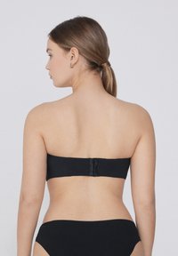 Černý bikiny top bez ramínek s hladkou texturou a zapínáním na zádech. Jednoduchý design, minimální akcenty a odpovídající černý spodní díl.