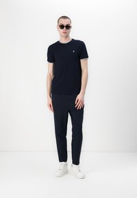 Námořnická modrá tričko s bílým lemem, doplněné námořnickými textured kalhotami a bílými teniskami. Modelka nosí kulaté černé sluneční brýle.