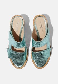 Metalni aqua sandali s dva široka remena, kožnom postavom i teksturiranom površinom. Imaju prirodni drveni potplat ukrašen dekorativnim zakovicama.