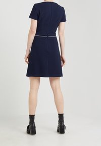 Robe en maille bleu marine à manches courtes, corsage cintré et jupe évasée. Dispose d'une fermeture éclair au dos et d'un passepoil blanc décoratif à la taille.