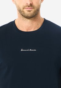Marineblaues kurzärmeliges T-Shirt aus weicher Baumwolle, mit einem weißen gestickten Logo auf der Brust, klassischem Rundhalsausschnitt und normaler Passform.