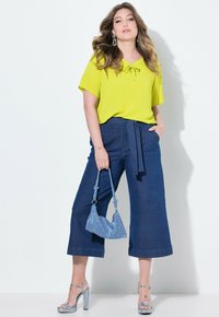 Limegrön blus med knytkrage, ihopparad med mörkblå vida byxor. Tillbehör inkluderar en glittrig blå handväska och silverfärgade klackar.