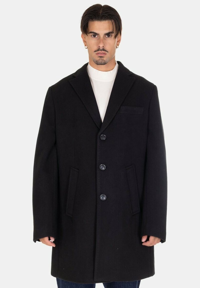 Cappotto in misto lana nera con colletto a revers, tre bottoni frontali, due tasche laterali e una tasca sul petto. Tessuto texturizzato.