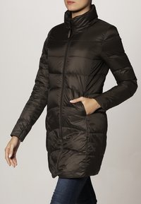 Mörkbrun pufferjacka med hög krage, långa ärmar, quiltat mönster och sidofickor, tillverkad av glänsande, isolerande material.