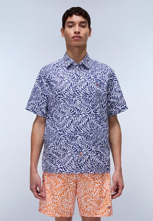 Chemise à manches courtes avec un motif tourbillon bleu marine et blanc, col boutonné, ornée d'un détail de bouton orange. Associée à un short à motifs orange et blanc.