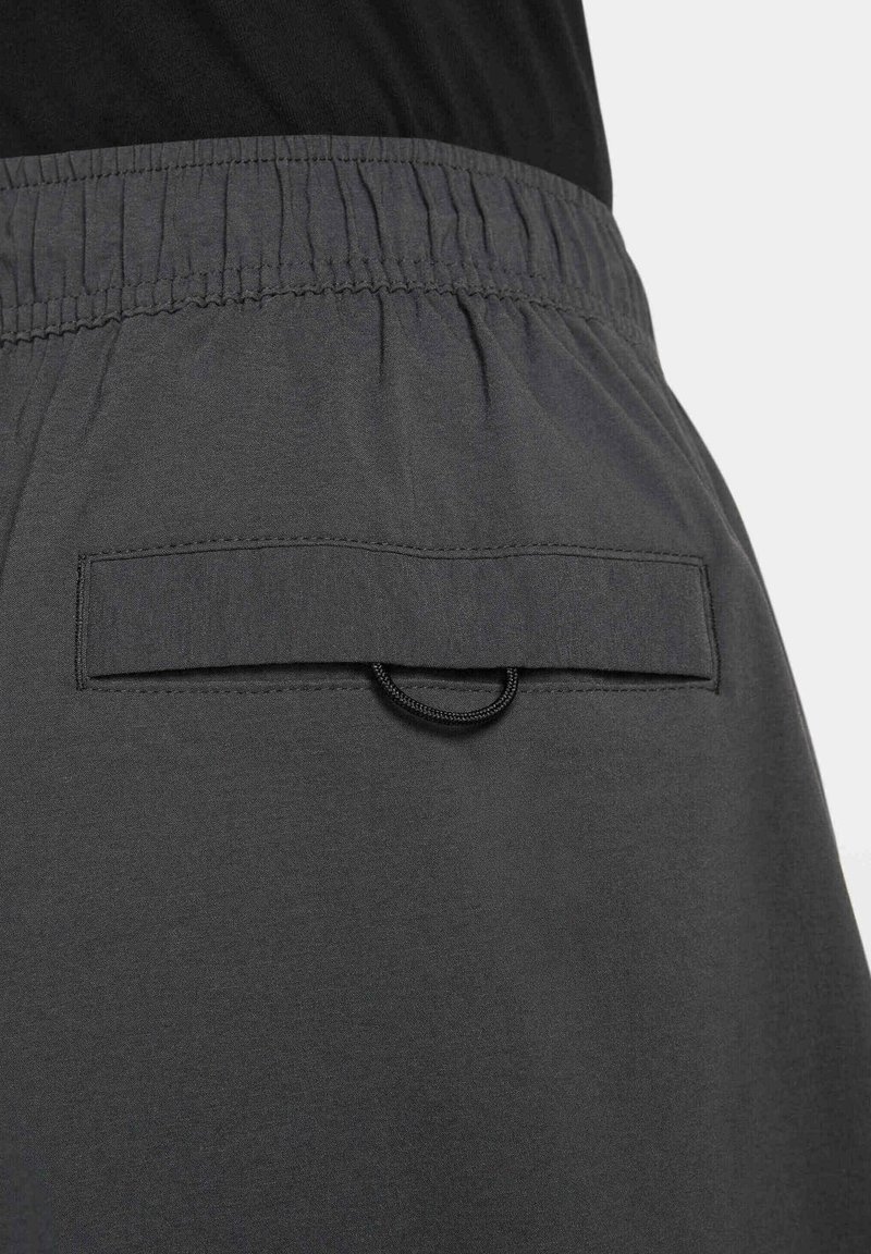 Pantalones cortos deportivos grises con una cintura elástica, que cuentan con un bolsillo trasero con tapa y un detalle de lazo. Textura suave y diseño minimalista.