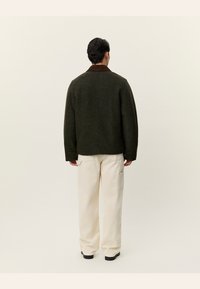 Tmavě zelený vlněný kabát s hnědým límcem, oversized střih, spadlé ramena a bílé cargo kalhoty. Jemná textura a minimalistický design.