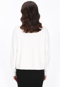 Weißer Strickpullover mit lockerer Passform und gerippten Bündchen, von hinten gezeigt. Glatte Textur, cropped Länge über einem schwarzen Rock.