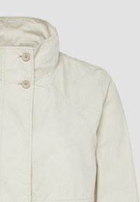 Licht beige jack met een hoge kraag, twee bruine knopen en subtiele stiksels. De stof lijkt glad met een licht matte afwerking.