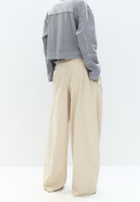 Giacca grigia corta con maniche lunghe, abbinata a pantaloni beige a gamba larga e ampi, entrambi caratterizzati da texture morbide e design minimalista.