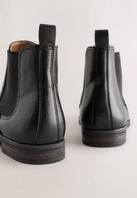 Zwarte leren Chelsea boots met elastische zijpanelen, een ronde neus, een gestructureerde afwerking en een klein hakje met houten accenten.