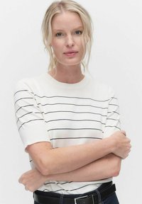 Hvid kortærmet sweater med vandrette marineblå striber og rund halsudskæring, parret med mørke jeans og et sort bælte.