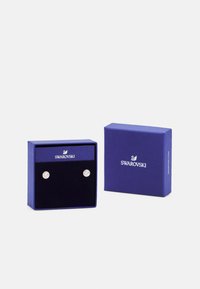Swarovski rotas dārglietu kārba zila ar teksturētu virsmu, kurā ir apaļi kristāla auskari uz melna samta iekšpuses.
