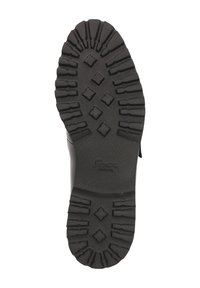 Zwarte rubberen zool met diepe noppen en diamantpatronen, met een gestructureerd oppervlak. De zool heeft zichtbare branding nabij de rand.