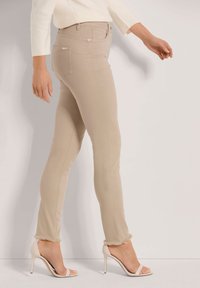 Beige fitted trousers with a frayed hem, made from a stretchy fabric. Paired with open-toed high-heeled shoes and a light sweater.