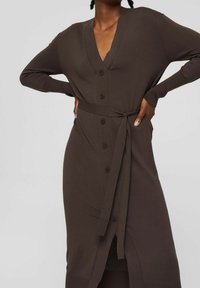 Brązowa dzianinowa sukienka kardiganowa z dekoltem w serek, sześcioma guzikami i materiałowym paskiem w talii. Długie rękawy i średniej długości krój.