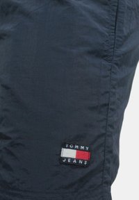 Pantalones cortos azul marino hechos de una tela ligera, con un logo rectangular bordado con acentos en rojo, blanco y azul en la pierna.
