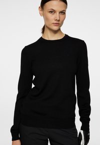 Svart stickad tröja med rund halsringning, figurnära design och långa ärmar. Har subtil logotypdetalj på bröstet och textil med struktur.