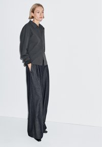Gray oversized shirt with a collar, paired with loose dark denim trousers. Soft texture, relaxed fit, and subtle striped detail at cuffs.