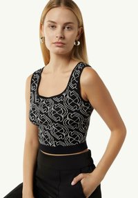 Schwarzes Strick-Crop-Top mit einem geometrischen weißen Muster, einem quadratischen Ausschnitt und einer taillierten Silhouette, kombiniert mit hochgeschnittenen schwarzen Hosen.