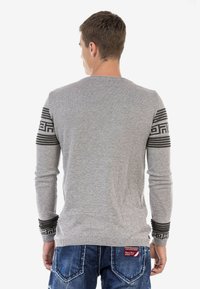 Grauer Pullover mit langen Ärmeln, ausgestattet mit schwarzen geometrischen Mustern auf den Schultern und gerippten Bündchen; aus einer Baumwollmischung.