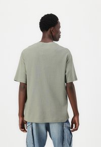 Olivgrön bomulls-t-shirt med korta ärmar, något texturerad tygkvalitet och rund halsringning, bärs tillsammans med ljusblå denim cargo-byxor.