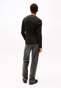 Schwarzes Langarmshirt kombiniert mit dunkler, verblasster Denim-Jeans. Das Shirt hat einen Rundhalsausschnitt; die Jeans sind gerade geschnitten und verfügen über Gesäßtaschen.