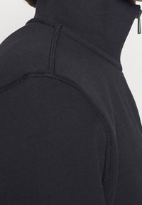 Svart höghalssk sweatshirt med en slät yta, med kontrasterande sömmar och dragkedjeslutning vid kragen.