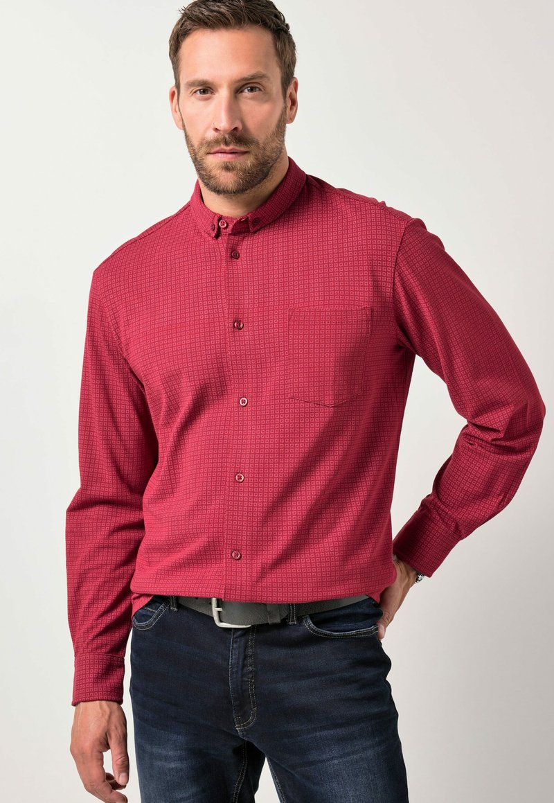 Rød mønstret skjorte med knapper, brystlomme og krave. Lange ærmer, lige pasform, lavet af et glat stof. Båret med mørke jeans.
