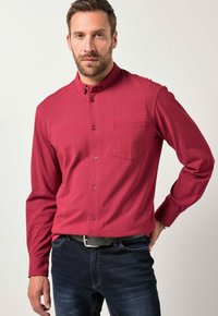 Rode geblokte button-up shirt met een borstzak en kraag. Lange mouwen, rechte pasvorm, gemaakt van een soepele stof. Draagt met een donkere spijkerbroek.
