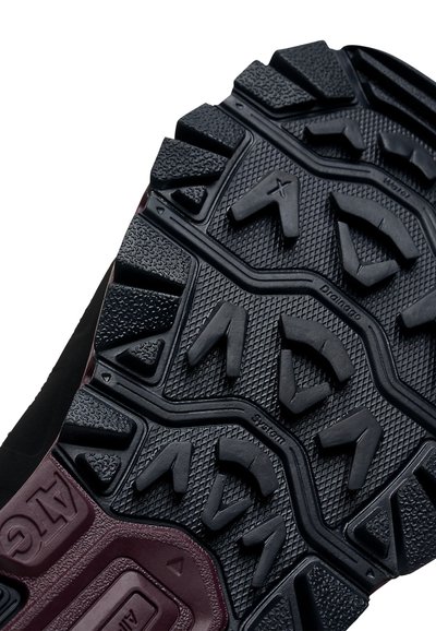 Semelle de chaussure de sport noire avec des crampons épais et multidirectionnels, des motifs texturés et des accents bordeaux dans la zone du talon.