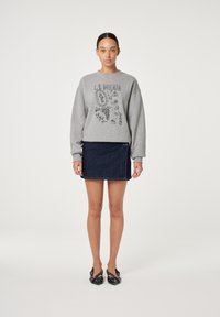 Grijze sweatshirt met zwarte grafische print en ronde hals, gecombineerd met een donkere denim minirok. Zwarte schoenen met een geweven textuur.