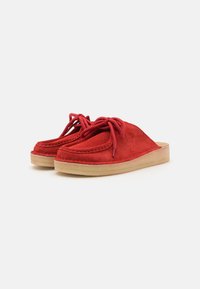 Red suede slip-on shoes with decorative laces, round toe, and contrasting beige rubber sole. Smooth texture and stitched accents.