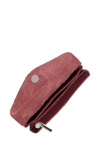 Czerwony zamszowy portfel o teksturowanym wykończeniu, z zamknięciem na zamek błyskawiczny i okrąłym metalowym akcentem. Kompaktowy design w kształcie trójkąta.