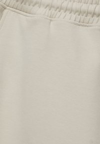 Ceinture élastique beige clair avec ourlet cousu sur tissu en coton doux, vue en gros plan.