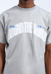 Camiseta de algodón gris con gran texto blanco "ALREDEDOR DEL MUNDO" y acentos azules con detalles de la marca, cuello redondo y mangas cortas.