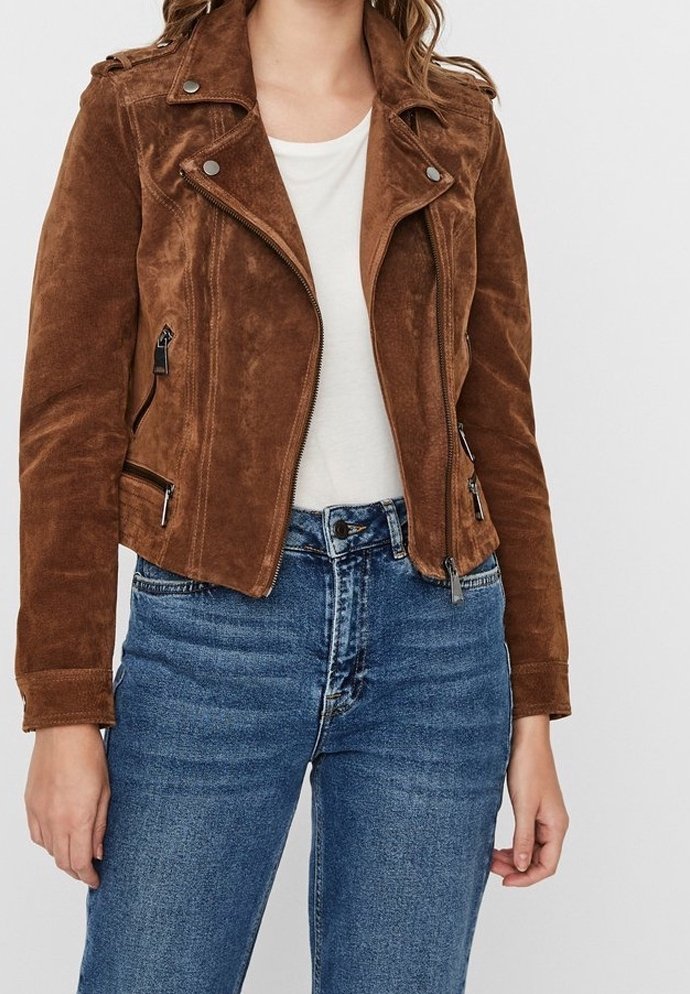 Femme portant une veste de motard en daim marron sur un haut blanc et un jean bleu, montrée des épaules aux hanches sur un fond uni.