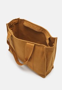 Bolsa de tela de color beige con dos asas resistentes, abertura superior y un bolsillo interior con cremallera. Presenta un acabado de tela texturizada.