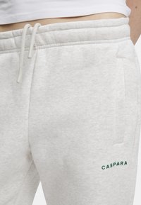 Vaaleanharmaat puuvillaiset collegehousut, joissa on sivutaskut, ribattu vyötärö ja nauhakiinnitys. "CASPARA" brodeerattu vihreänä lahkeessa.