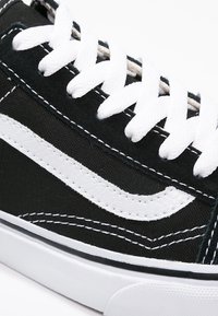 Svart canvas sneakers med vita snören, med en vit sidremsa och kontrasterande sömmar. Gummisula med texturerad yta.