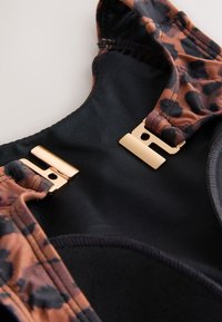 Leopard print straps in brown and black attached to a black fabric base, featuring gold metal hardware. Smooth texture, adjustable design.