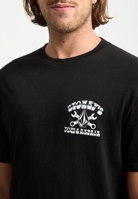 Czarny bawełniany t-shirt z białym logo graficznym przedstawiającym klucze i diamentowy kształt, oznaczony napisem "STONEY'S TOW & REPAIR." Gładka tekstura.