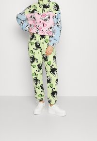 Farbenfrohes zwei-teiliges Loungewear-Set mit einem Halb-Reißverschluss-Oberteil in Pink, Blau und Grün sowie grünen Hosen mit einem schwarz-weißen Cartoon-Hundedarstellung.